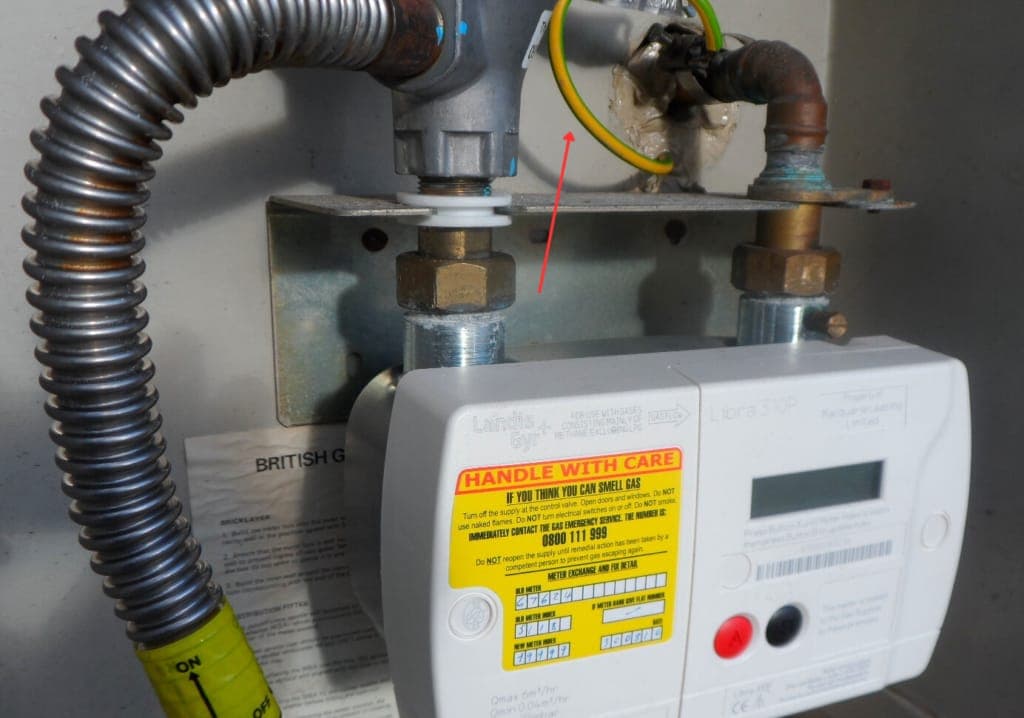 Gas meter with bonding clamp and yellow/green bonding cable, red arrow highlighting the clamp