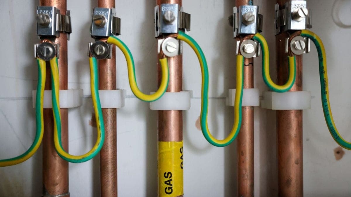 Multiple copper service pipes with bonding clamps and green/yellow bonding cable, including labelled gas pipe