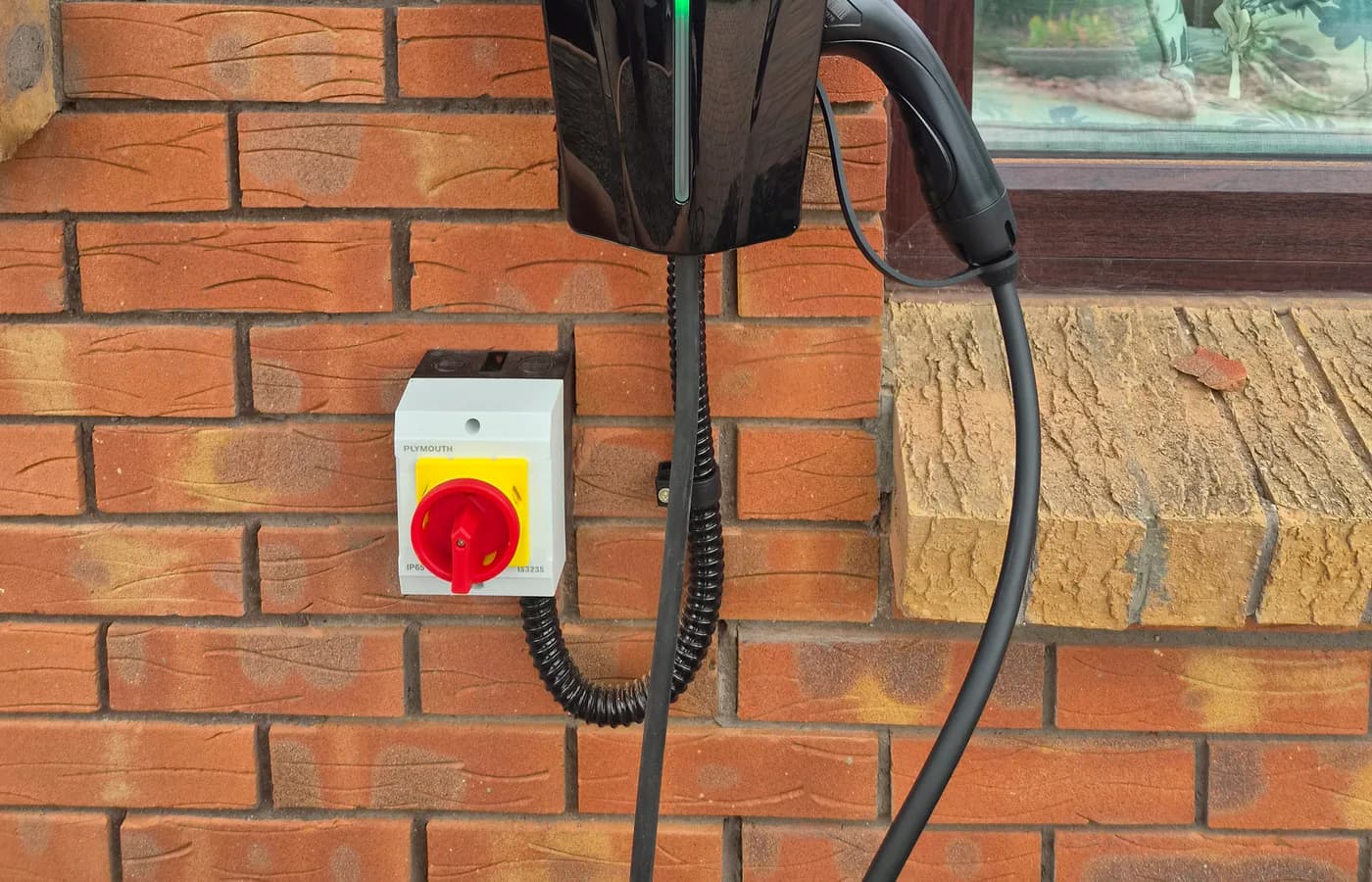 BENY home EV charger installed on an exterior brick wall with isolator switch and tethered Type 2 cable.